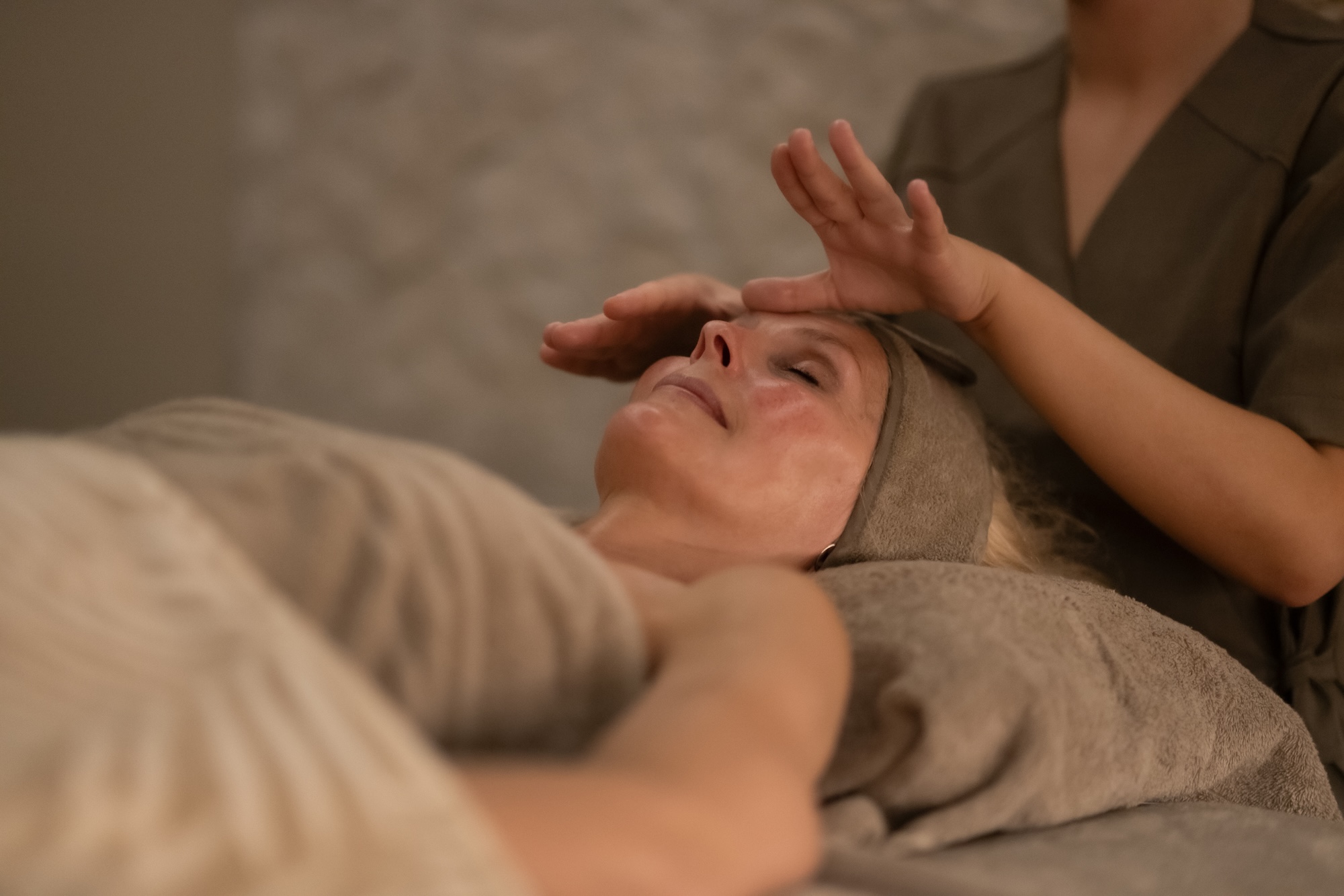 Person lying down with eyes closed during a spa facial, a therapist's hands gently cradle the head for a massage.